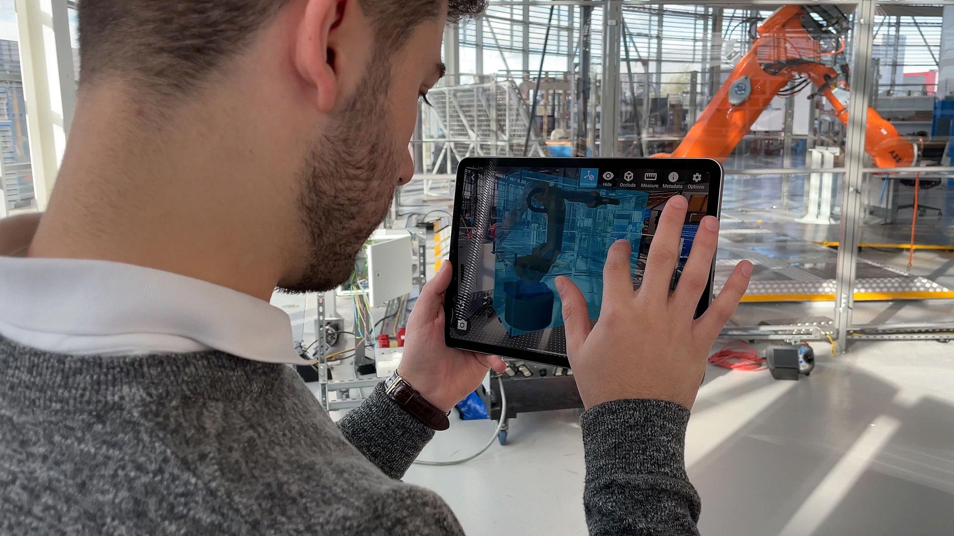 Engineer holding a tablet to visualize a robot arm in an empty cell.