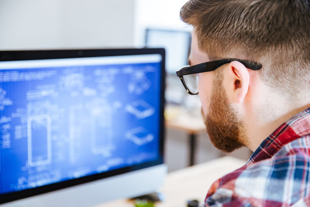 Closeup of young man in glasses with beard making blueprints on computer